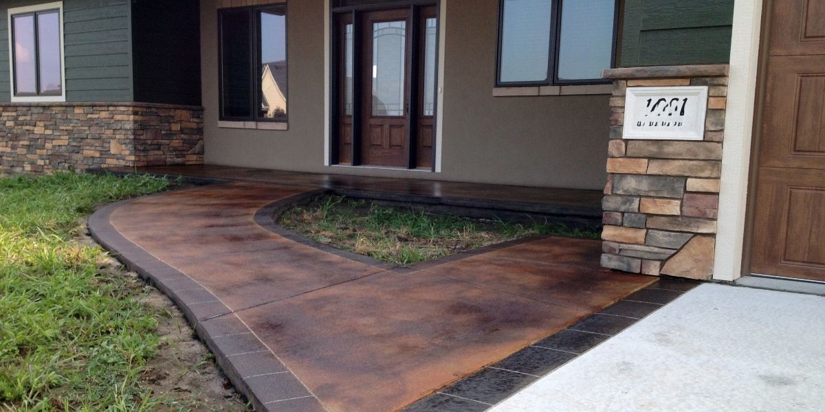 Warm stained and engraved concrete walkway leading to a home entrance