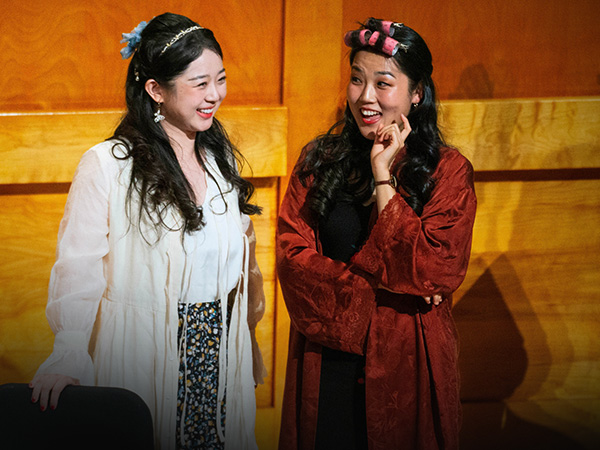Two female students with robes on, acting and singing on a stage.