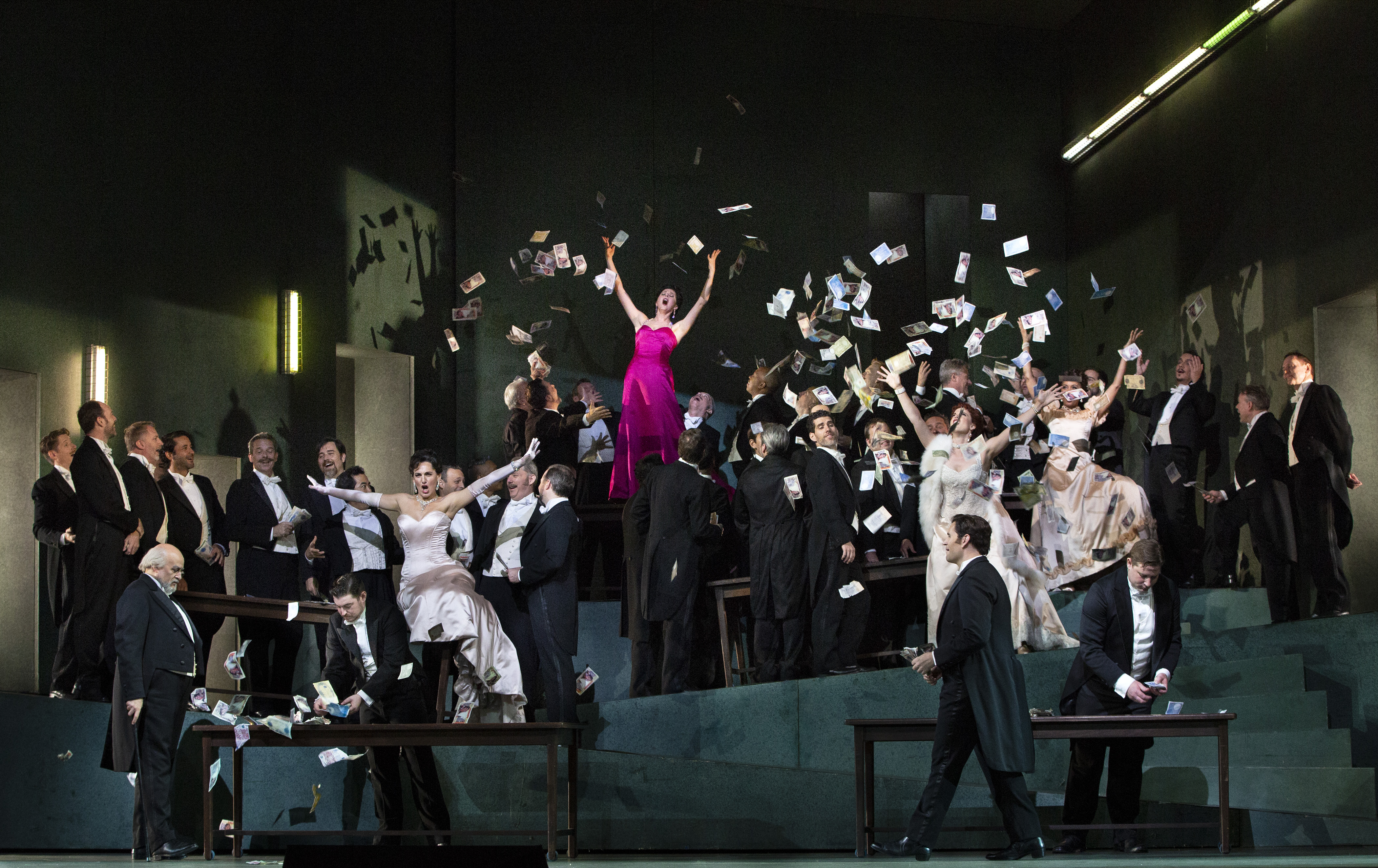 The Met Opera's cast of Manon. Woman in pink dress with her arms up in the air singing.
