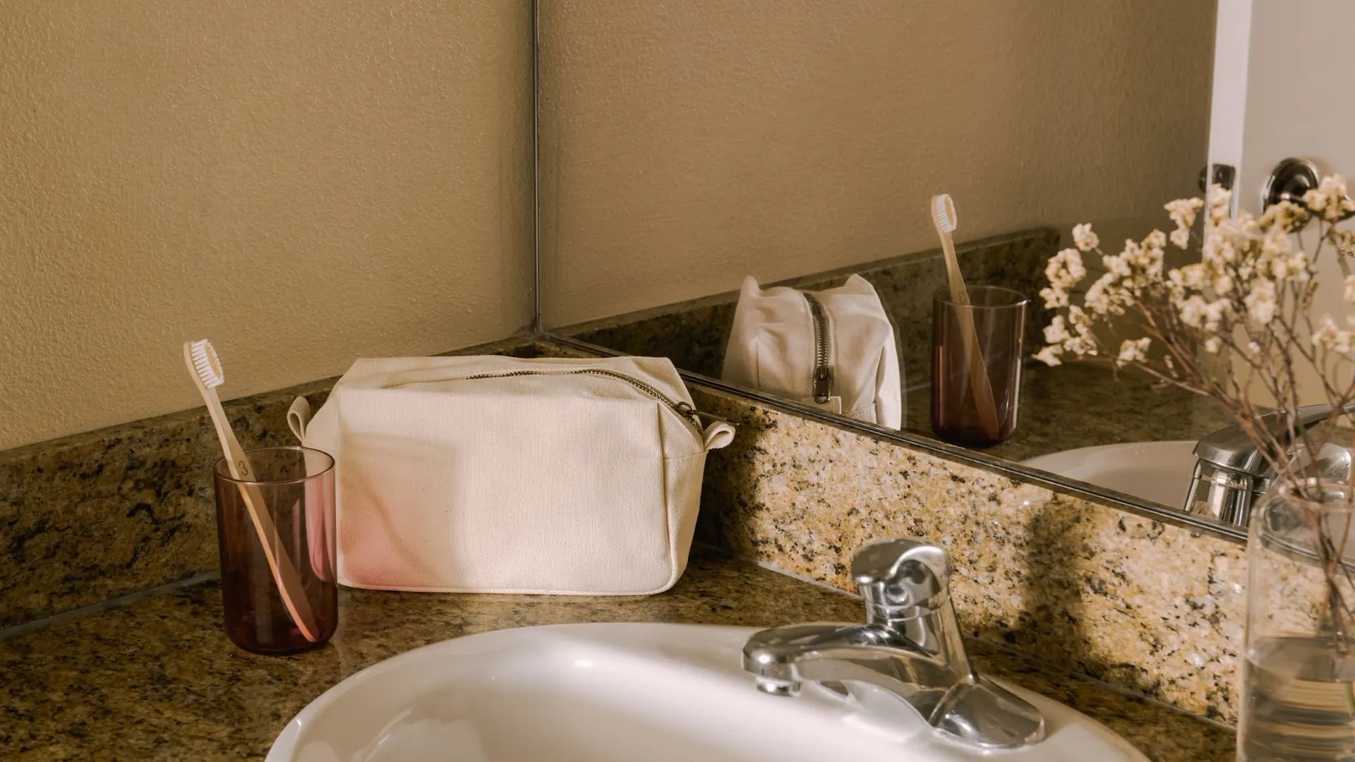 A bathroom sink with a granite countertop, white sink, and silver faucet, with a mirror and toiletries.