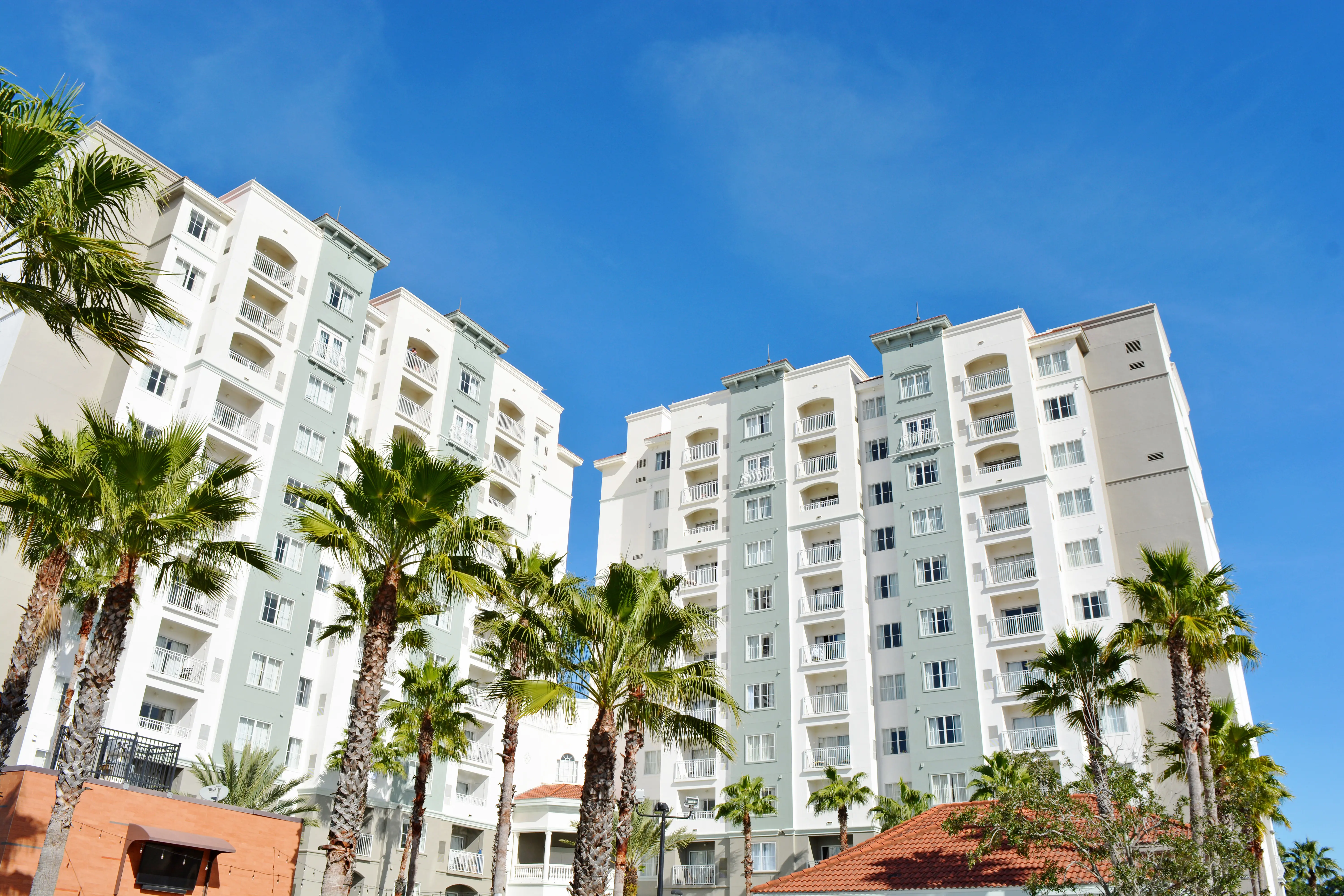 A large white building with balconies and palm trees in front of it.