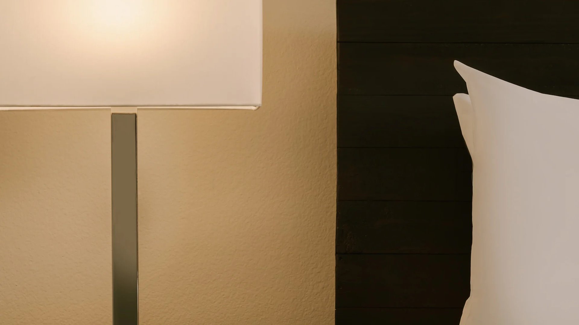 A close-up of a bed with a white pillow and a lamp beside it.